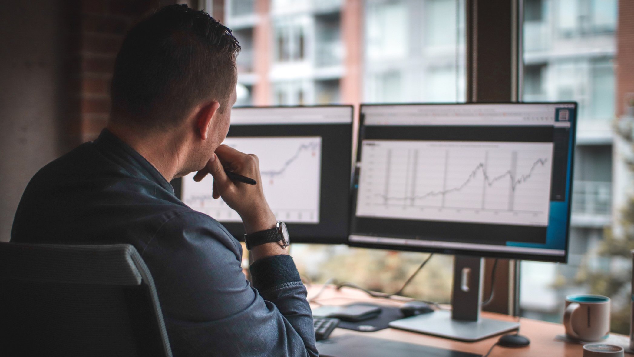 Man looking at computer screens with graphs